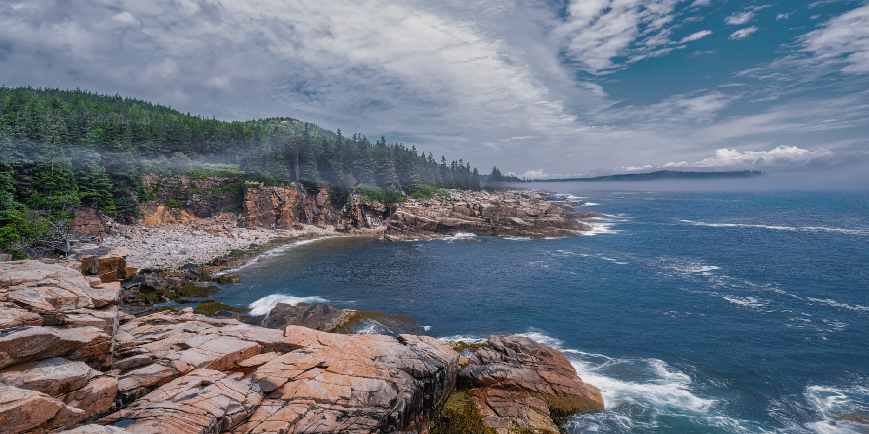A scenic coastal view with rocky cliffs, crashing waves, and a misty forest in the background.