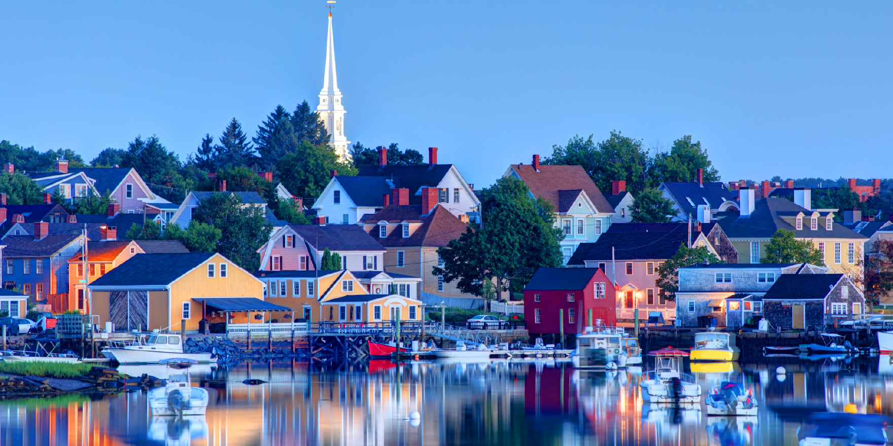 A colorful town with a church steeple overlooking a harbor.